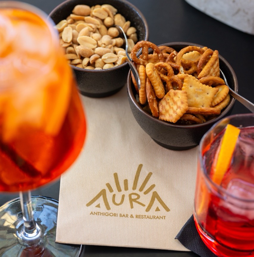 Aperitivo scene with cocktails, nuts and AURA branded napkin