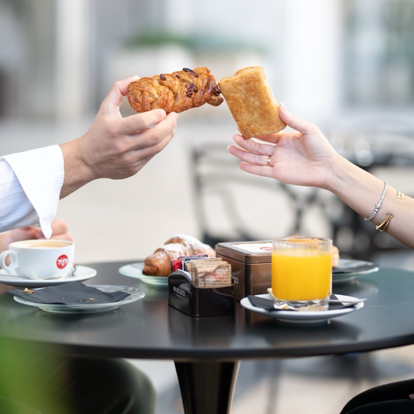 Hands sharing croissants over breakfast table with coffee and orange juice