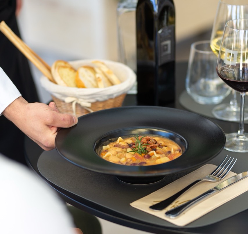 Server presenting elegant pasta dish with wine and bread