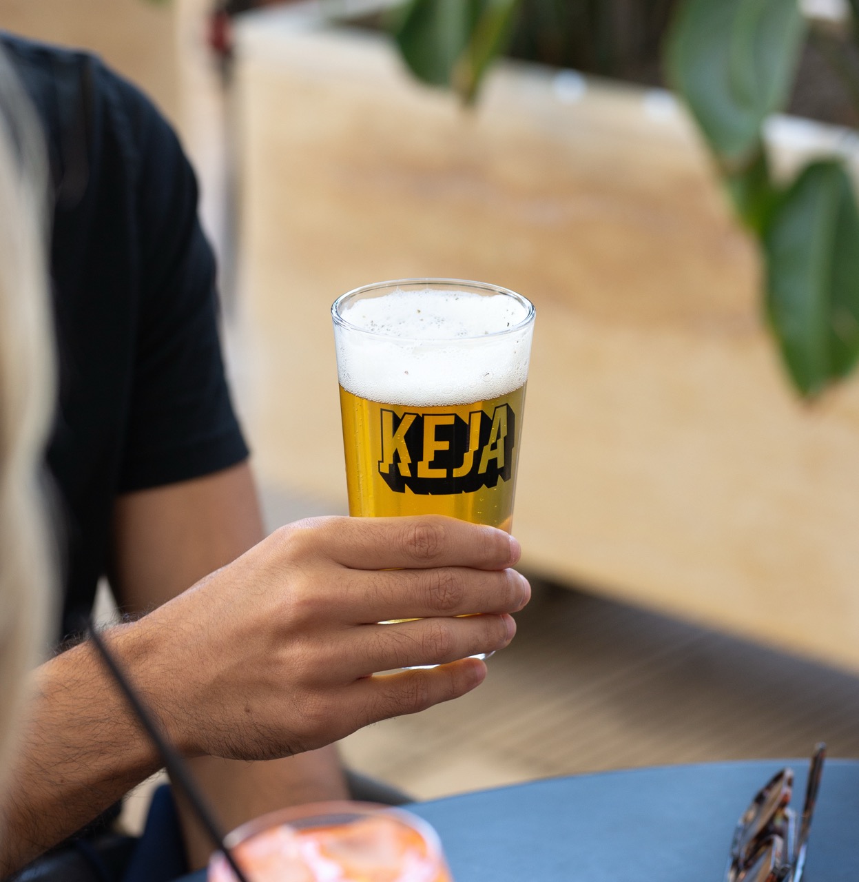 KEJA beer glass held in hand with outdoor restaurant setting